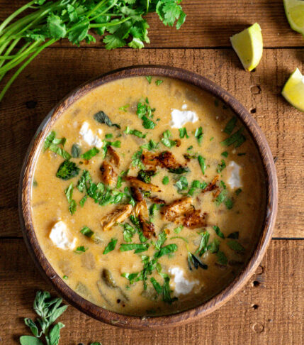 A bowl of vegan white chicken chili with cilantro, oregano, and limes on the table