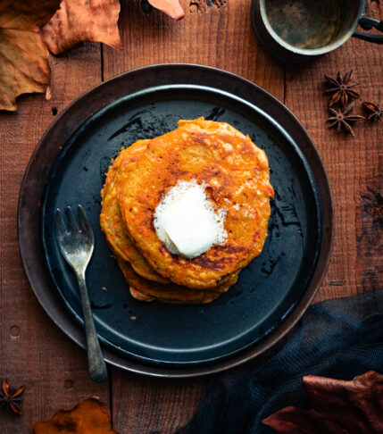 ginger carrot pancakes stacked on a black plate surrounded by leaves