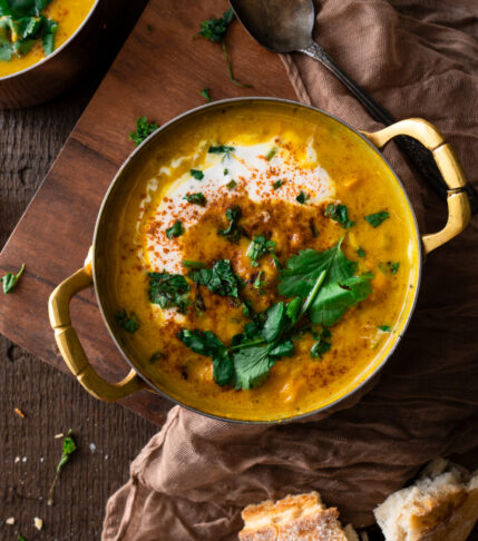 two bowls of Golden turmeric lentil and sweet potato soup with bread and cilantro