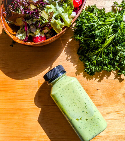 A bottle of silken tofu green goddess dressing next to a salad and parsley